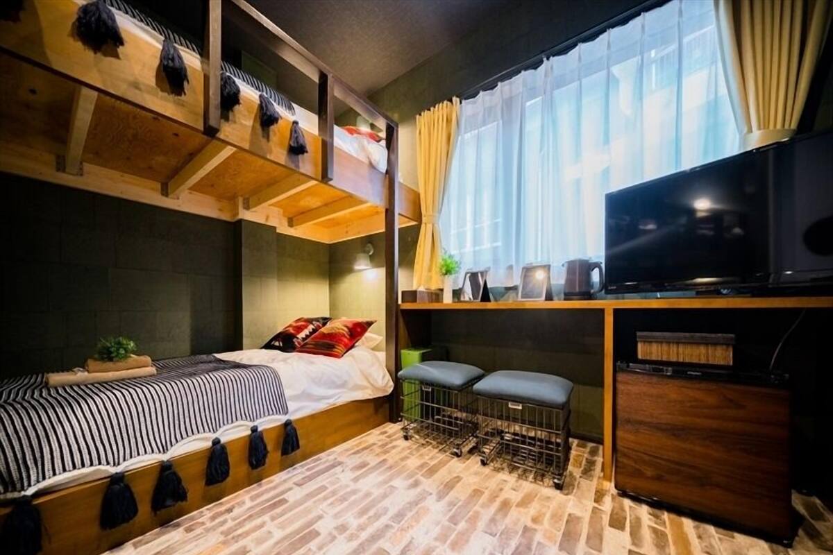 Una habitación compacta con cama, televisión, un pequeño rincón de descanso y ventana con cortinas.