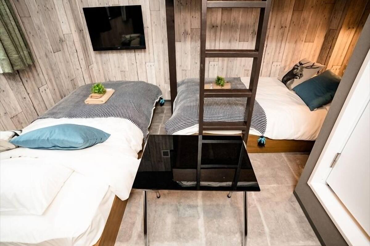Habitación compacta con dos camas, un televisor montado en la pared y una escalera.