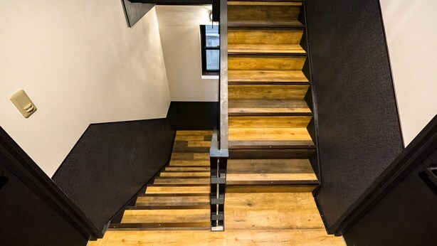 A staircase with wooden steps and black railings, leading to a landing with a small window. - IKIDANE Residential Hotel Komagome (Tokyo)