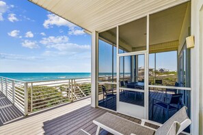 A covered outdoor area with a view of the beach, featuring a wooden deck, glass doors, and outdoor furniture. - EXPERIENCE THE ULTIMATE IN ISLAND LIVING at the incredible beach front home AMBASSADOR. (St. George Island)