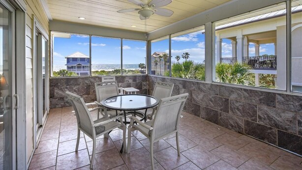 A covered patio with a round table and chairs, a ceiling fan, and large windows offering a view of the ocean and buildings. - A MEMORY OF A LIFETIME is what you will have when you stay at this beautiful Plantation home (St. George Island)