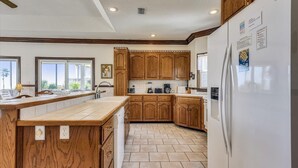A kitchen with wooden cabinets, a white refrigerator, and a large window. - A MEMORY OF A LIFETIME is what you will have when you stay at this beautiful Plantation home (St. George Island)