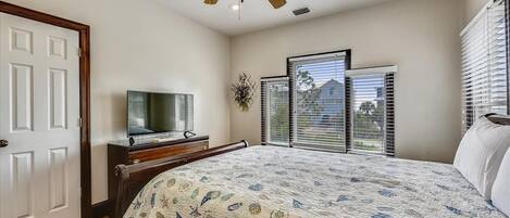 A bedroom with a bed, a ceiling fan, a television on a dresser, and a window with blinds.