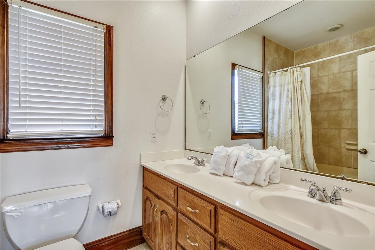 A bathroom with a toilet, two sinks, a mirror, and a shower curtain.