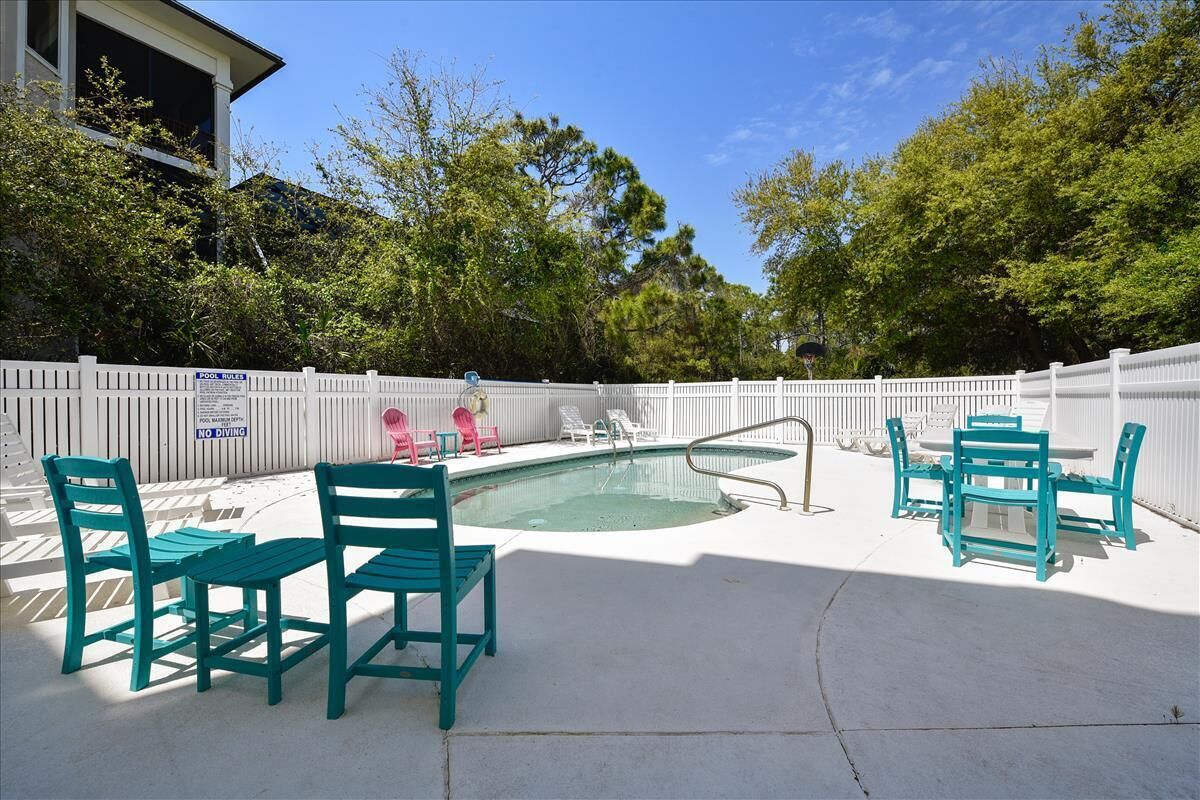 A backyard with a swimming pool, surrounded by a white fence, and featuring outdoor furniture.