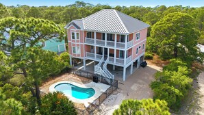 A two-story house with a balcony, a swimming pool, and surrounded by trees.