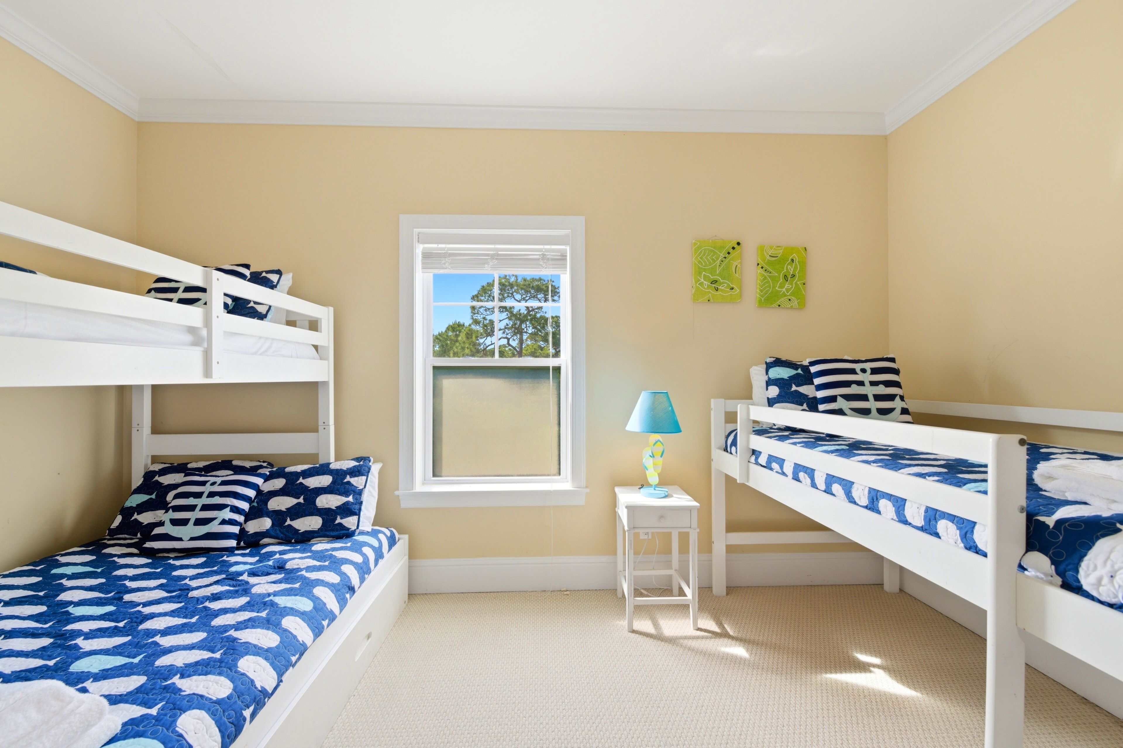 A room with bunk beds, a window, a lamp, and two wall decorations.