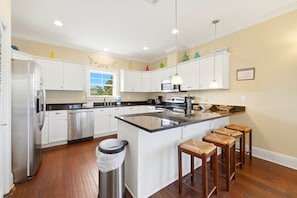 Uma cozinha moderna com armários brancos, uma geladeira de aço inoxidável, uma ilha grande com banquetas e uma janela com vista.