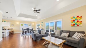 A spacious living area with hardwood flooring, a gray sofa set, a wooden coffee table, and a ceiling fan.