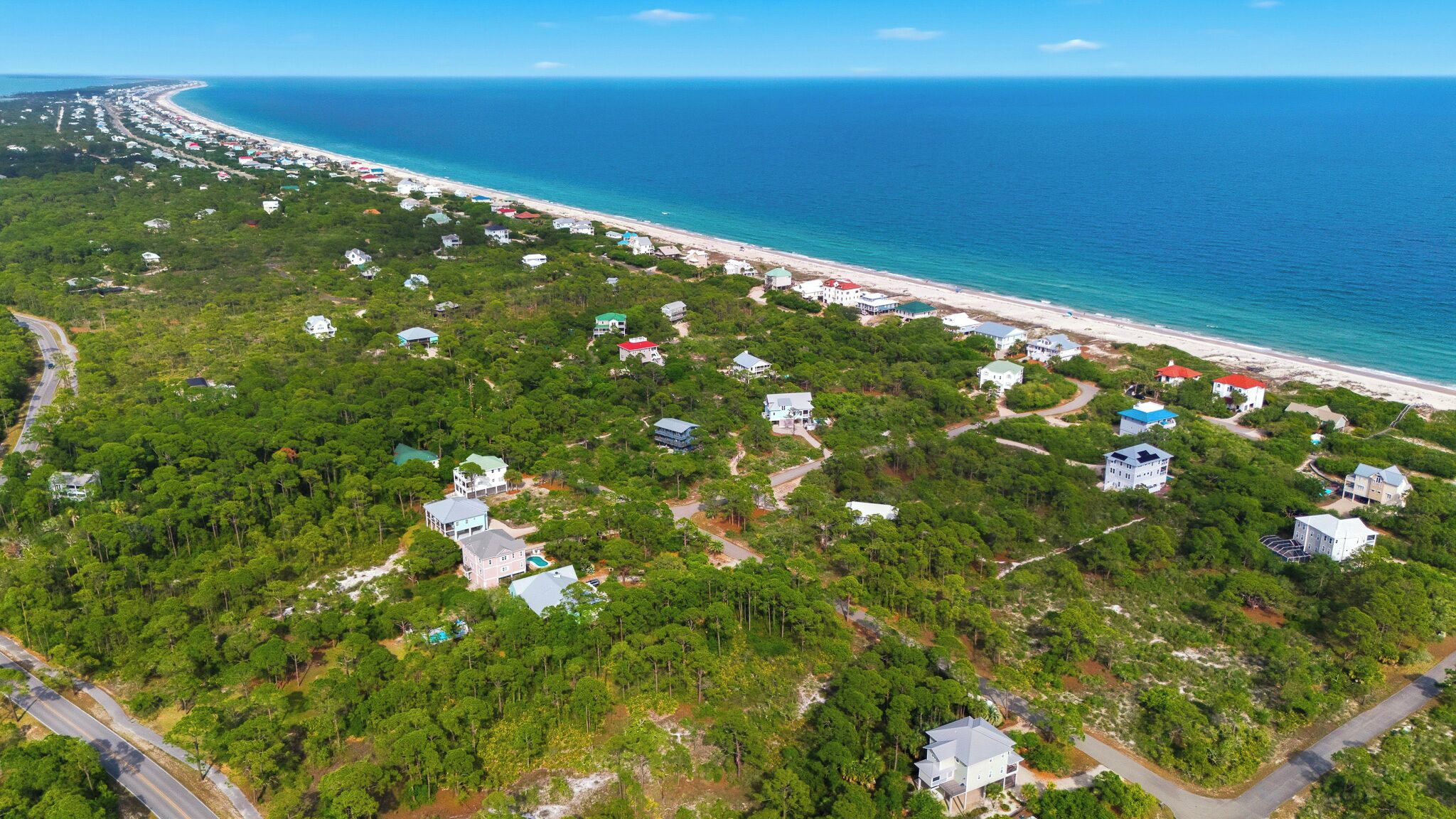 An aerial view of a coastal area with houses, roads, and a beach.