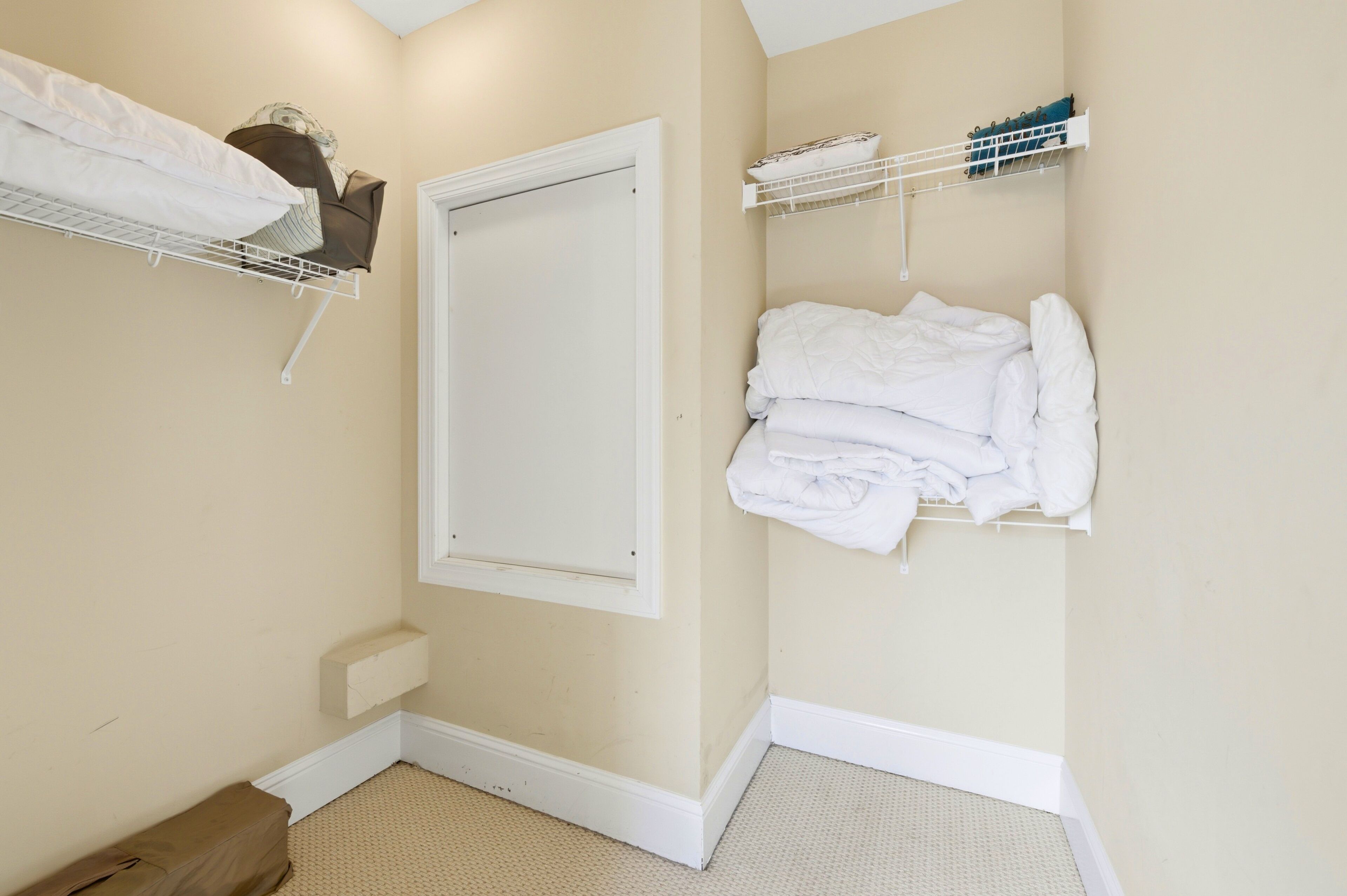 A small room with a door, a white shelf with folded towels, and a white shelf with bottles.