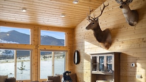 Enjoy a serene mountain view from the comfort of this cozy room, featuring a mounted deer and dog head, a leather sofa, and a cabinet with glass doors.