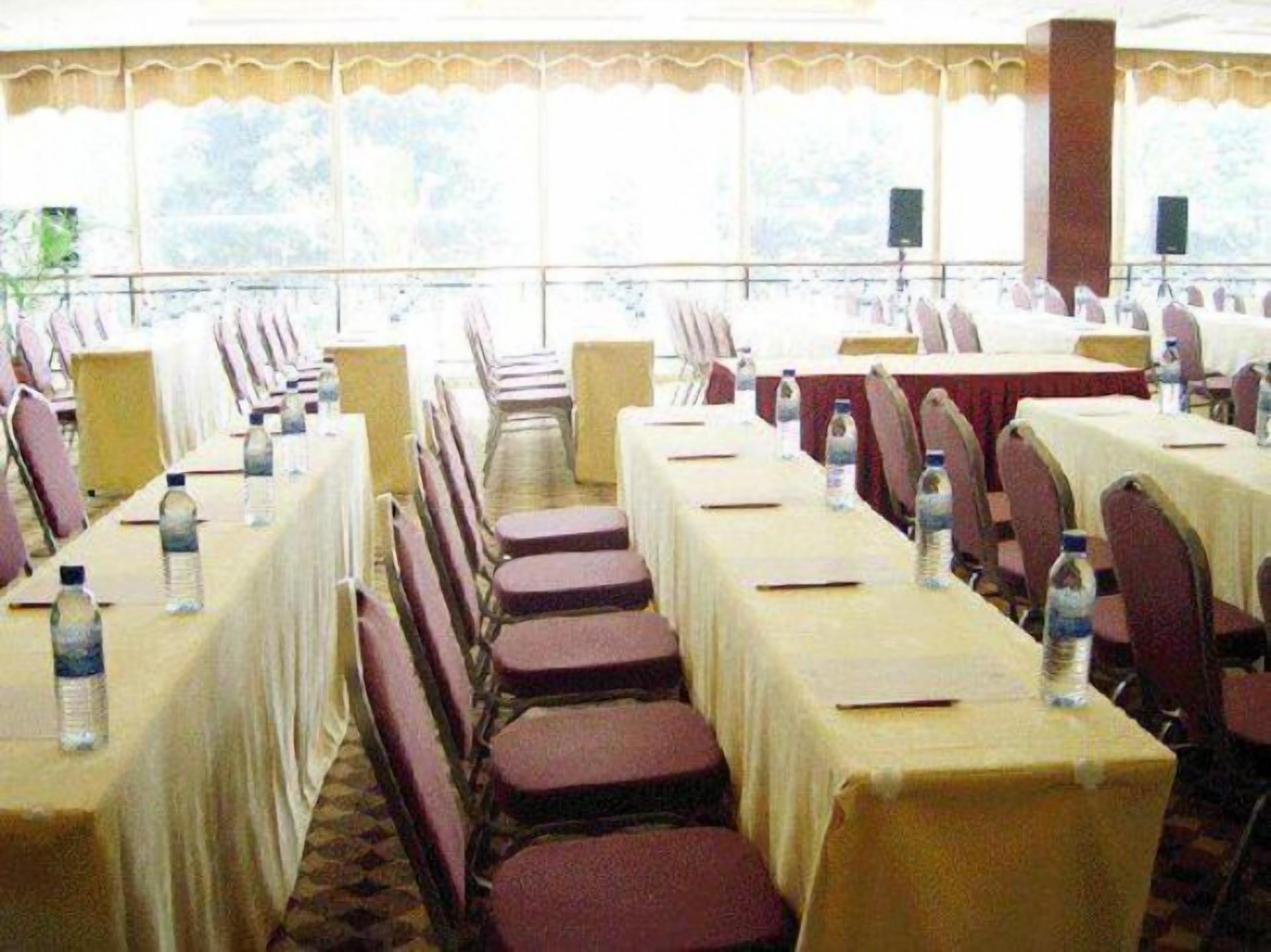 A conference room with rows of tables and chairs, each table with a bottle of water.