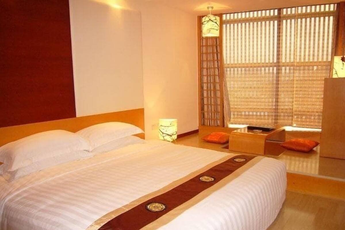 Een hotelkamer met een groot bed, een nachtkastje, een stoel en een raam met jaloezieën.
