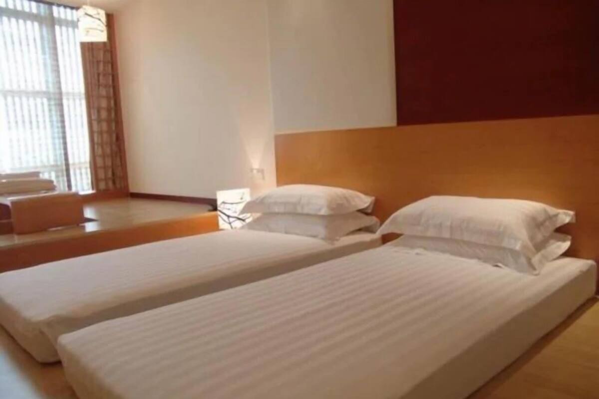 Een hotelkamer met twee eenpersoonsbedden, een houten hoofdbord en een groot raam met jaloezieën.
