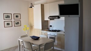 A compact kitchen with a gas stove, oven, and a mounted TV. There is a dining table with chairs and a fan. - PioppiHouse Casa Vacanza.  Large independent suite with small terrace overlooking the sea (Acciaroli)