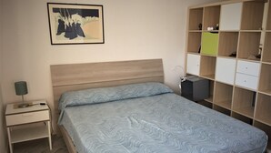 A bedroom with a bed, a nightstand, a bedside table, a lamp, a wall-mounted shelf, and a framed picture. - PioppiHouse Casa Vacanza.  Large independent suite with small terrace overlooking the sea (Acciaroli)