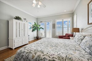 A bedroom with a large bed, a white dresser, a red chair, and a ceiling fan.