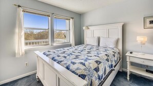Un dormitorio con cama, mesita de noche, ventana con cortinas y ventilador de techo.