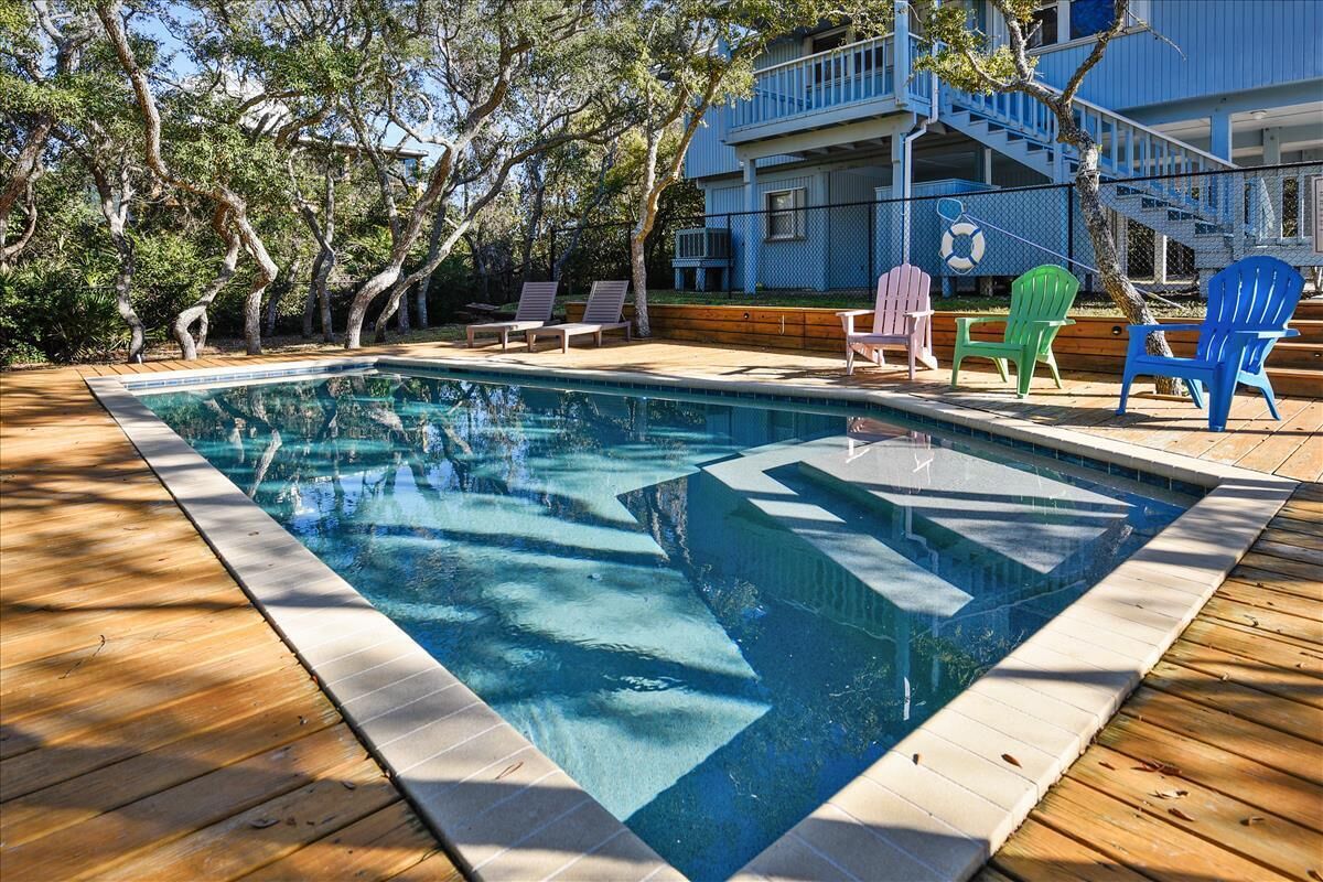 Ein Swimmingpool mit Holzdeck, umgeben von Bäumen und einem blauen Gebäude mit Balkon.