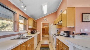 Una cocina moderna con armarios de madera, encimera blanca, microondas, estufa y cafetera.
