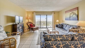 Una sala de estar con un sofá, sillones, televisión y vistas al exterior a través de un ventanal.