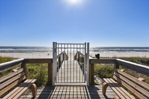 A wooden boardwalk leading to a beach with a clear sky.
