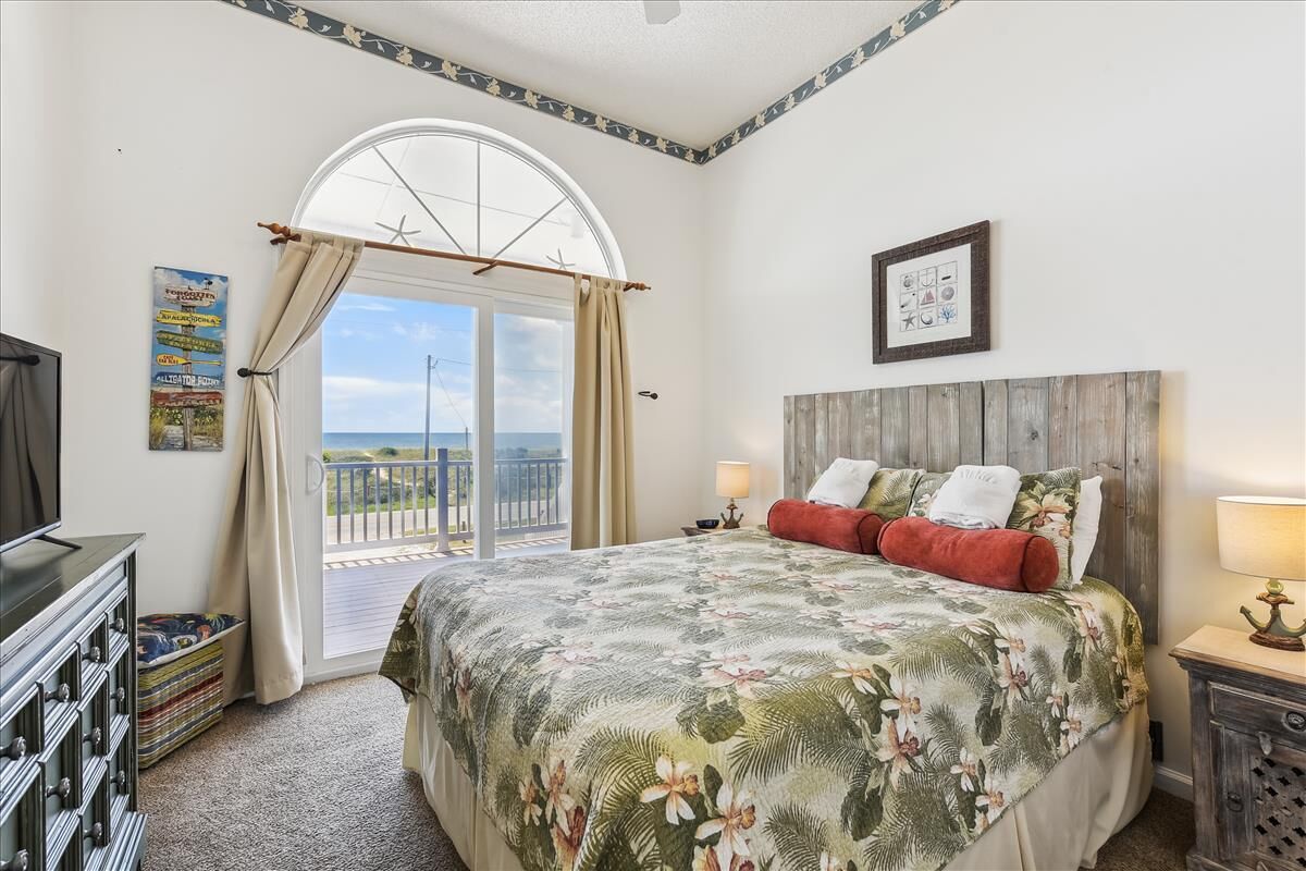 A bedroom with a large bed, a TV, a wooden headboard, and a balcony with a view.