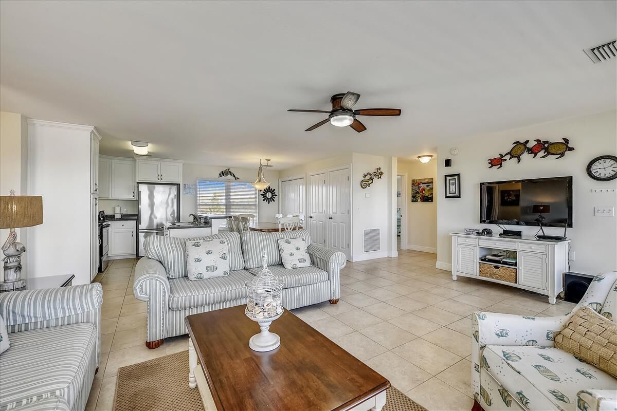 A living room with striped sofas, a wooden coffee table, a ceiling fan, and a TV on a white cabinet.