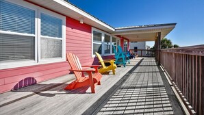 File di poltrone Adirondack colorate su un molo di legno, di fronte a un edificio rosso con rifiniture bianche e ampie finestre.