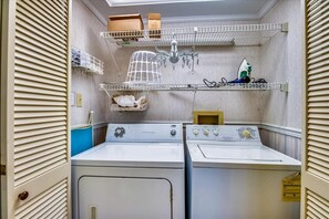Un cuarto de lavandería con dos lavadoras y secadoras, estantes con cajas de almacenamiento, un tendedero y una araña.