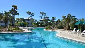A swimming pool with lounge chairs and umbrellas, surrounded by palm trees and a building in the background. - BIRD WATCHER IS PARADISE FOR A NATURE LOVER!! (St. George Island)