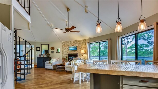 A spacious kitchen with a large island, a dining area with white chairs, a fireplace, and a view through large windows. - BIRD WATCHER IS PARADISE FOR A NATURE LOVER!! (St. George Island)