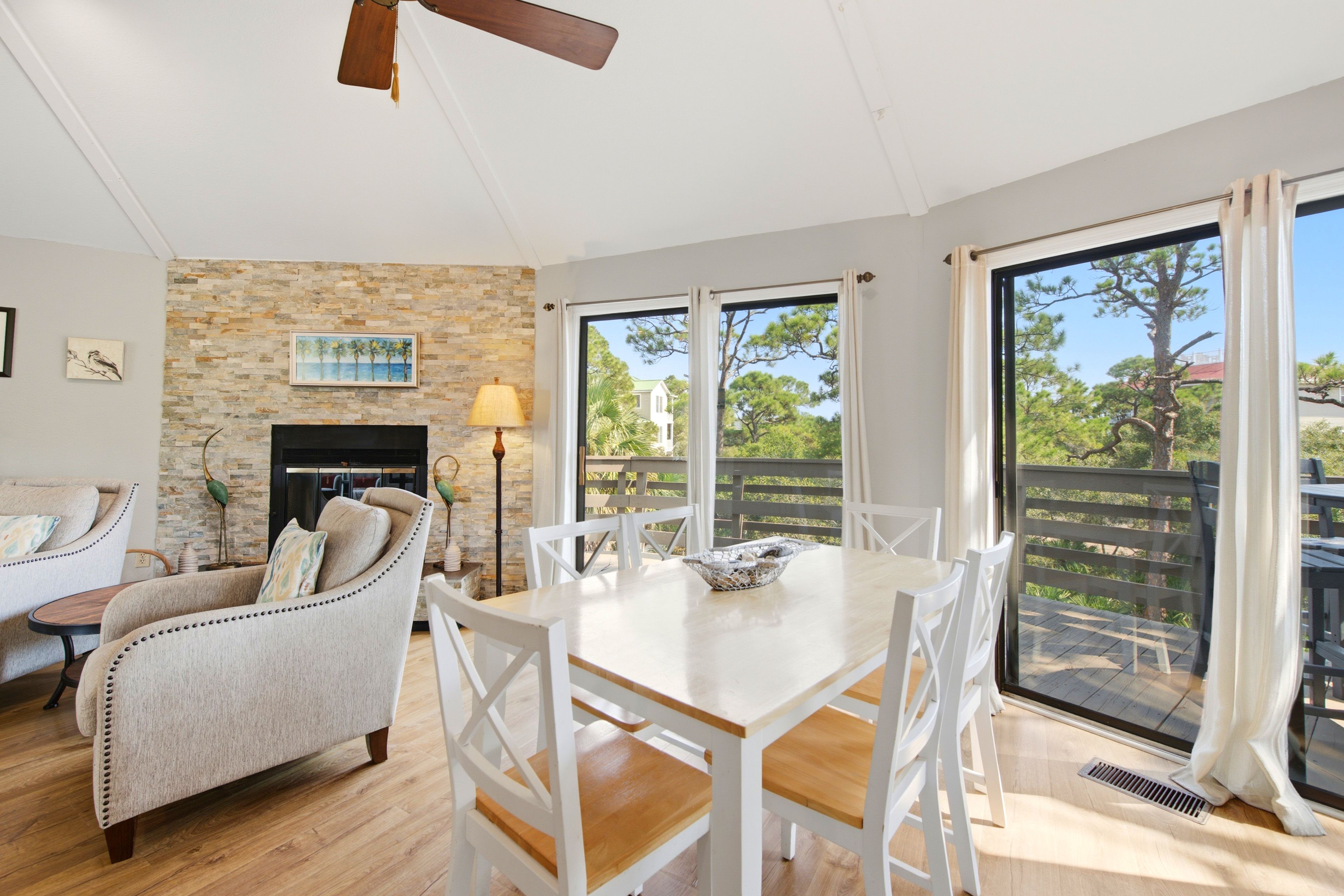 A spacious living area with a fireplace, a dining table with chairs, and a view of the outdoors through large windows.