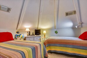 Una habitación con dos camas, un aparador, un televisor y una mesita de noche con lámpara.