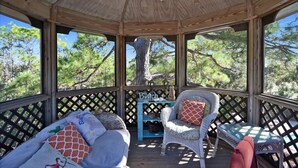 A covered outdoor seating area with wicker furniture and a small table, surrounded by a wooden lattice fence. - BIRD WATCHER IS PARADISE FOR A NATURE LOVER!! (St. George Island)