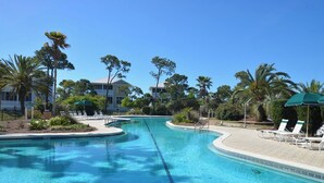 A clear swimming pool with lounge chairs and umbrellas, surrounded by palm trees and a building in the background. - THIS FABULOUS FIRST-TIER PLANTATION property is the ultimate family gathering place! (St. George Island)