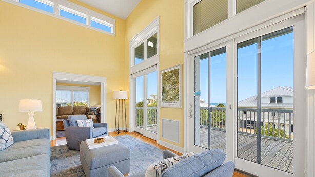 A spacious living room with a large sliding glass door to a deck, a sofa set, and a lamp. - THIS FABULOUS FIRST-TIER PLANTATION property is the ultimate family gathering place! (St. George Island)