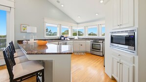 A modern kitchen with white cabinets, a granite countertop, stainless steel appliances, and a dining area with a bench. - THIS FABULOUS FIRST-TIER PLANTATION property is the ultimate family gathering place! (St. George Island)