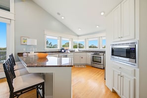 Una cocina moderna con armarios blancos, encimera de granito, electrodomésticos de acero inoxidable y un comedor con banco.