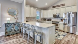 Cozinha moderna com armários brancos, uma ilha central com banquetas, eletrodomésticos de aço inoxidável e um espelho decorativo.