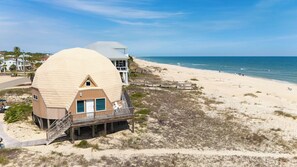 A beach house with a large dome structure, a wooden deck, and a view of the ocean.