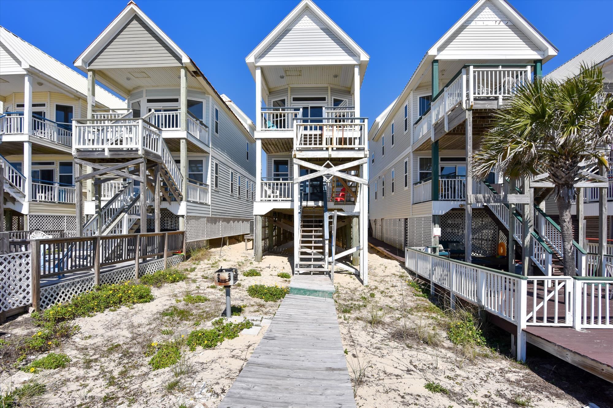 A beachfront hotel with multiple balconies, a central staircase, and a wooden walkway leading to the beach.