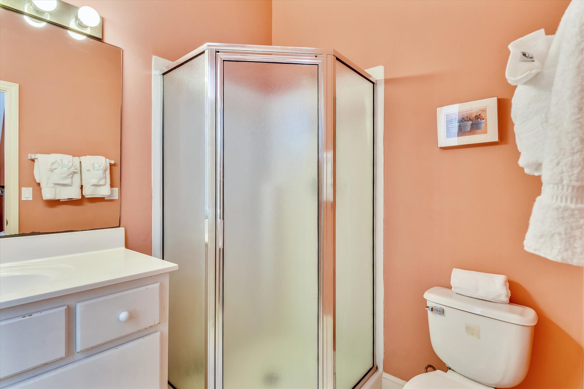 A bathroom with a glass-enclosed shower, white sink, and toilet.