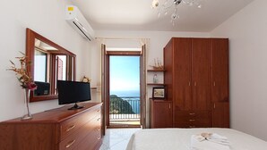 Een slaapkamer met een bed, een televisie op een houten dressoir, een garderobe en een balkon met uitzicht.