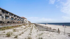 Hotel ved stranden med flere balkoner, en sandstrand i forgrunden og havet i baggrunden.