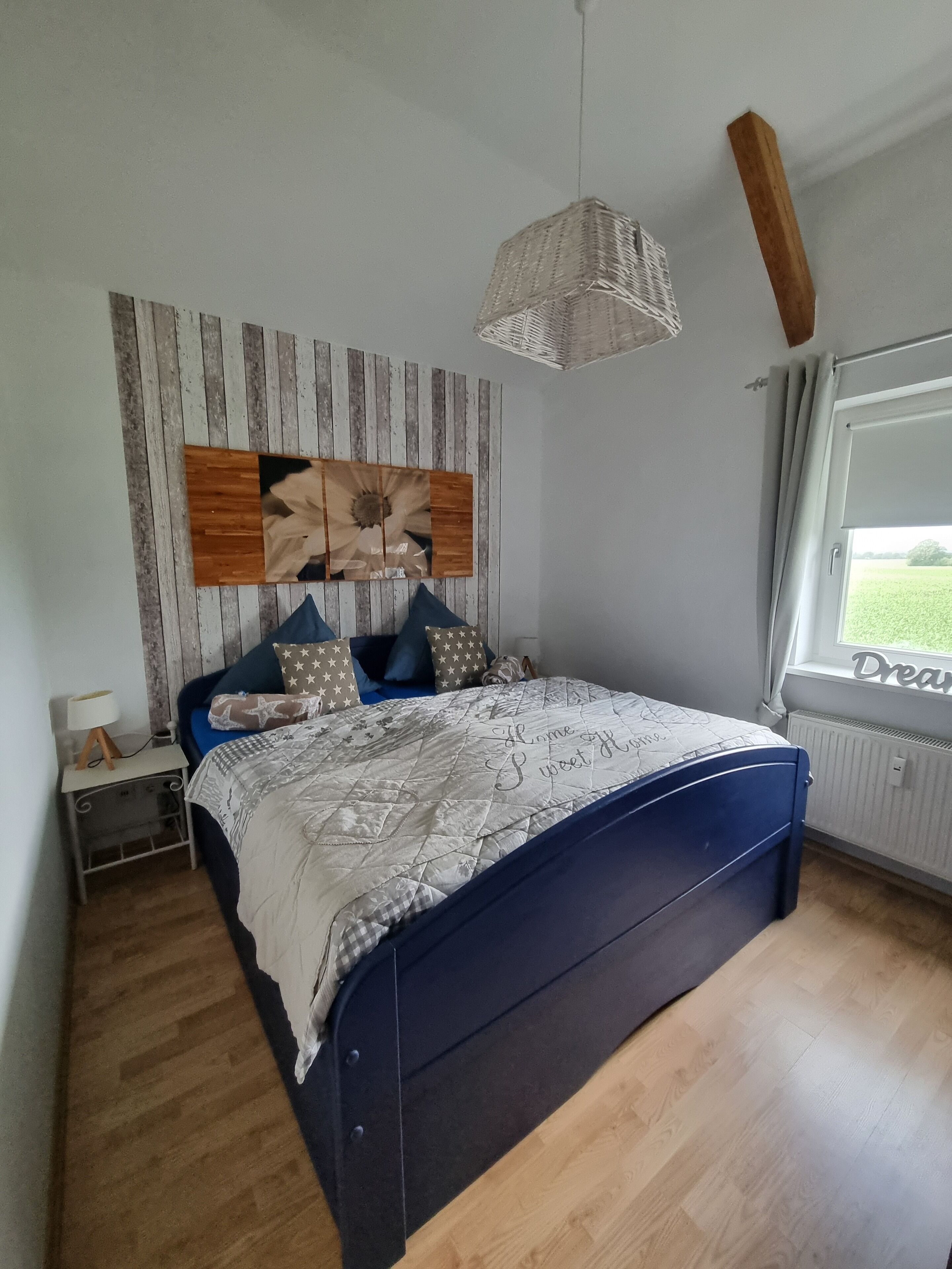 Une chambre avec un lit, une table de chevet, un luminaire suspendu, une fenêtre donnant sur un beau paysage et un mur orné d’un panneau en bois.