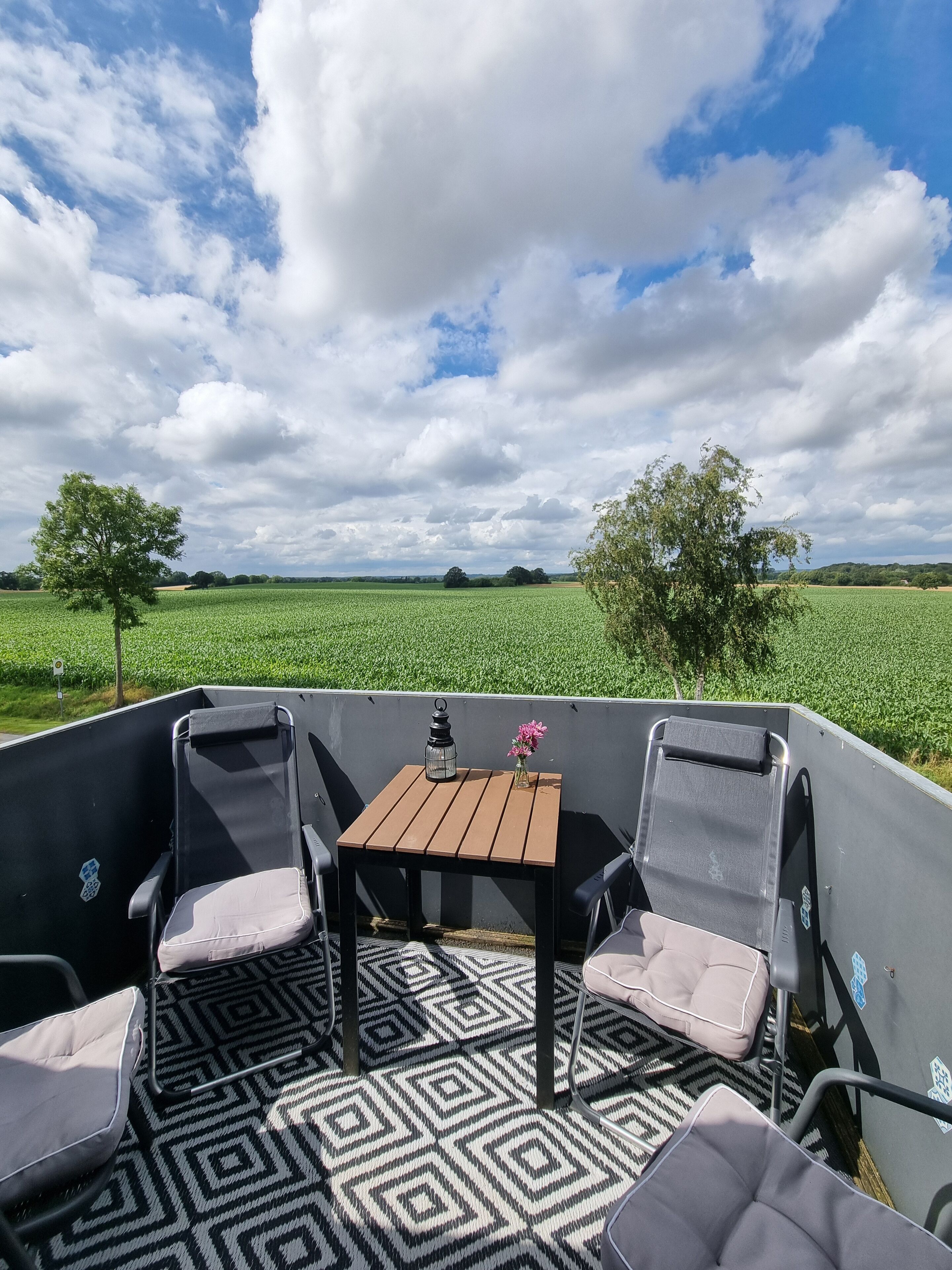 Eine Terrasse mit Tisch, Stühlen, einer Laterne und einem Blumenvasen.