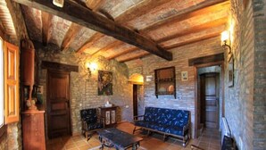 Ein rustikaler Innenraum mit freiliegenden Holzbalken, Steinwänden und einem gemusterten Sofa.