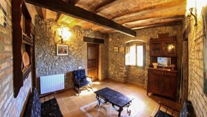 Ein rustikaler Raum mit Steinwänden, Holzbalkendecke, einem Tisch, einem Stuhl und einem Schrank.